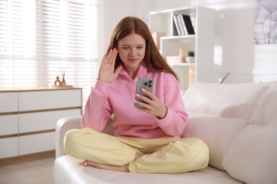 Photo of Beautiful teenage girl having videocall by smartphone on sofa at home