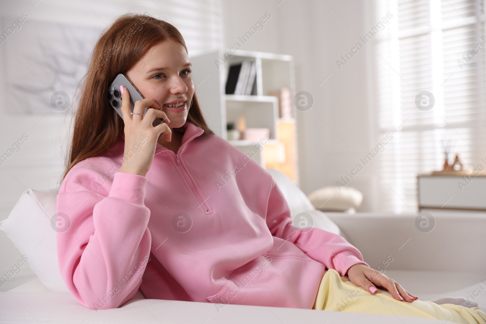 Photo of Smiling teenage girl talking by smartphone on sofa at home