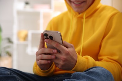 Photo of Smiling teenage boy using smartphone at home, closeup