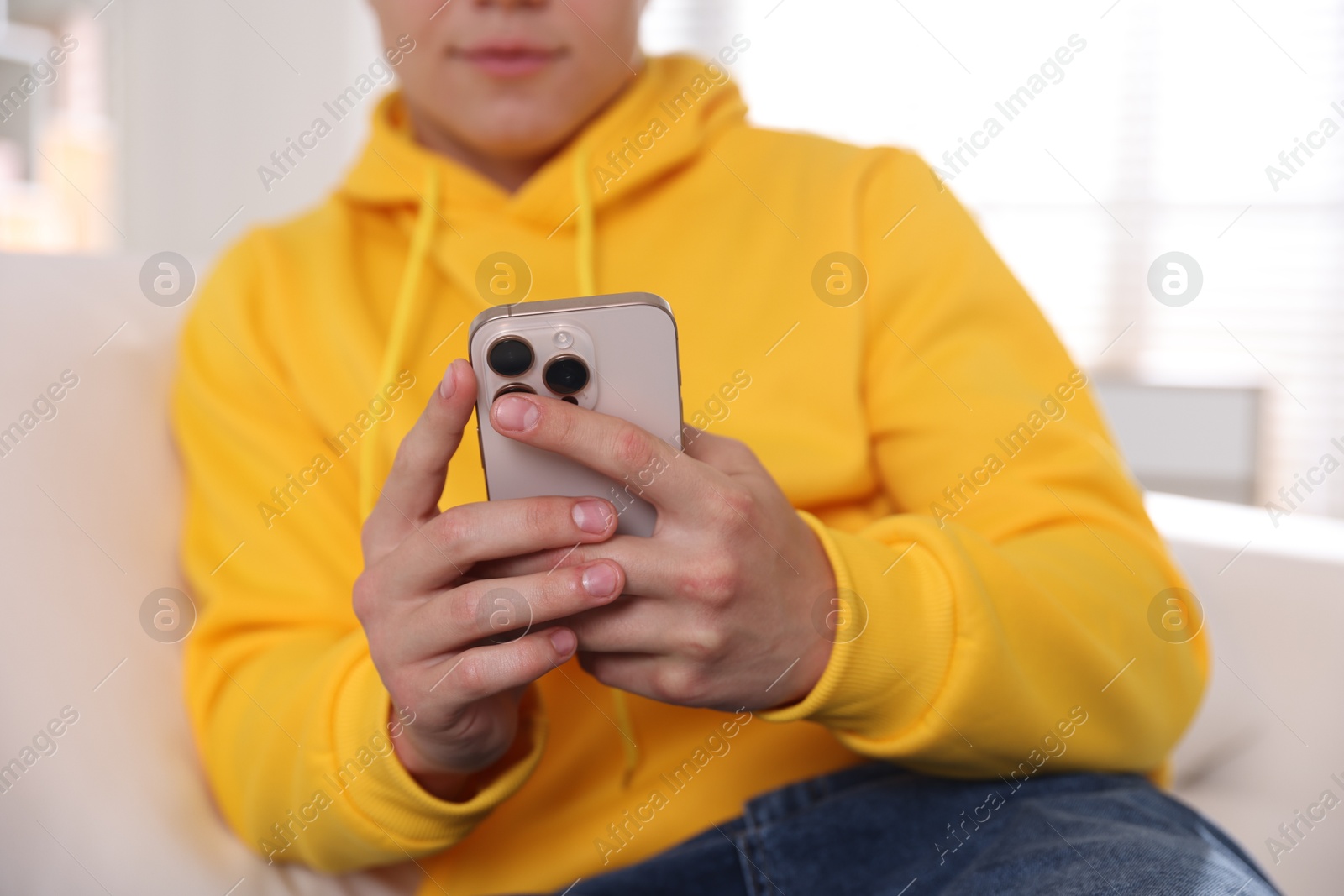 Photo of Teenage boy using smartphone at home, closeup