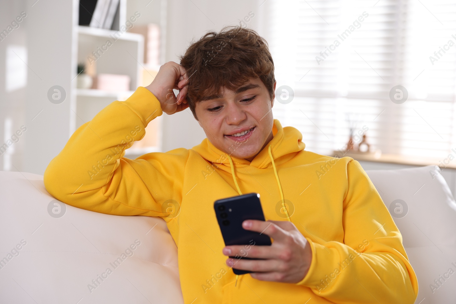 Photo of Smiling teenage boy using smartphone on sofa at home