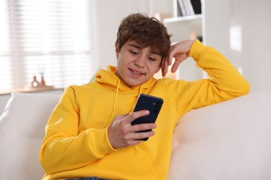 Photo of Smiling teenage boy using smartphone on sofa at home