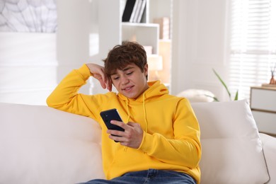 Photo of Smiling teenage boy using smartphone on sofa at home