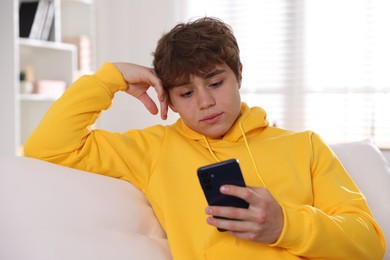 Photo of Teenage boy using smartphone on sofa at home
