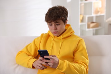 Photo of Teenage boy using smartphone on sofa at home