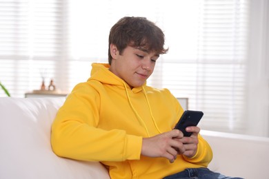 Photo of Teenage boy using smartphone on sofa at home