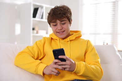 Photo of Smiling teenage boy using smartphone on sofa at home