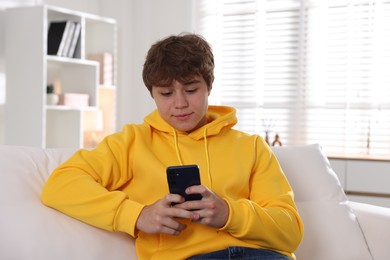 Photo of Teenage boy using smartphone on sofa at home