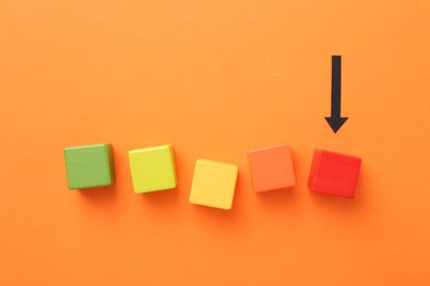 Photo of Maximum. Colorful cubes and arrow pointing at red one on orange background, flat lay