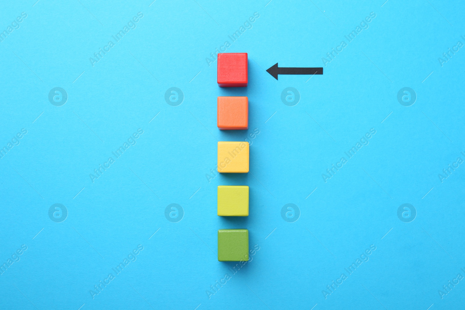 Maximum. Colorful cubes and arrow pointing at red one on light blue background, flat lay Photo of Maximum. Colorful cubes and arrow pointing at red one on light blue background, flat lay
