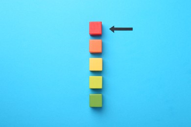 Photo of Maximum. Colorful cubes and arrow pointing at red one on light blue background, flat lay
