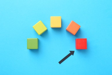 Photo of Maximum. Colorful cubes and arrow pointing at red one on light blue background, flat lay