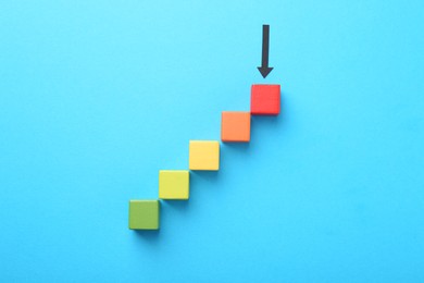 Photo of Maximum. Colorful cubes and arrow pointing at red one on light blue background, flat lay