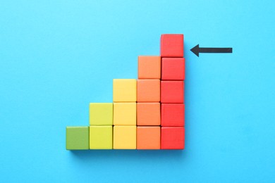 Photo of Maximum. Colorful cubes and arrow pointing at red one on light blue background, flat lay