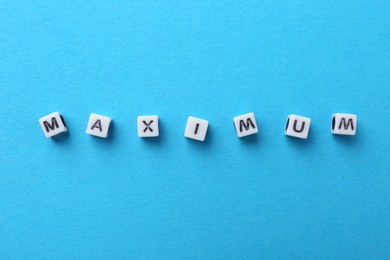 Photo of Word Maximum made of beads with letters on light blue background, top view