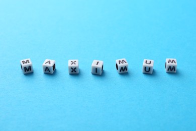 Photo of Word Maximum made of beads with letters on light blue background, closeup