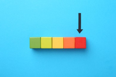 Photo of Maximum. Colorful cubes and arrow pointing at red one on light blue background, flat lay