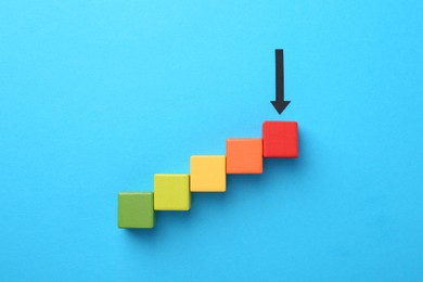 Photo of Maximum. Colorful cubes and arrow pointing at red one on light blue background, flat lay