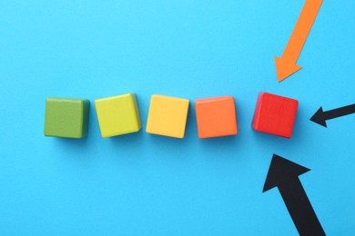 Photo of Maximum. Colorful cubes and arrows pointing at red one on light blue background, flat lay