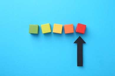 Photo of Maximum. Colorful cubes and arrow pointing at red one on light blue background, flat lay