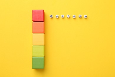 Photo of Colorful cubes and word Maximum made of beads with letters on yellow background, flat lay
