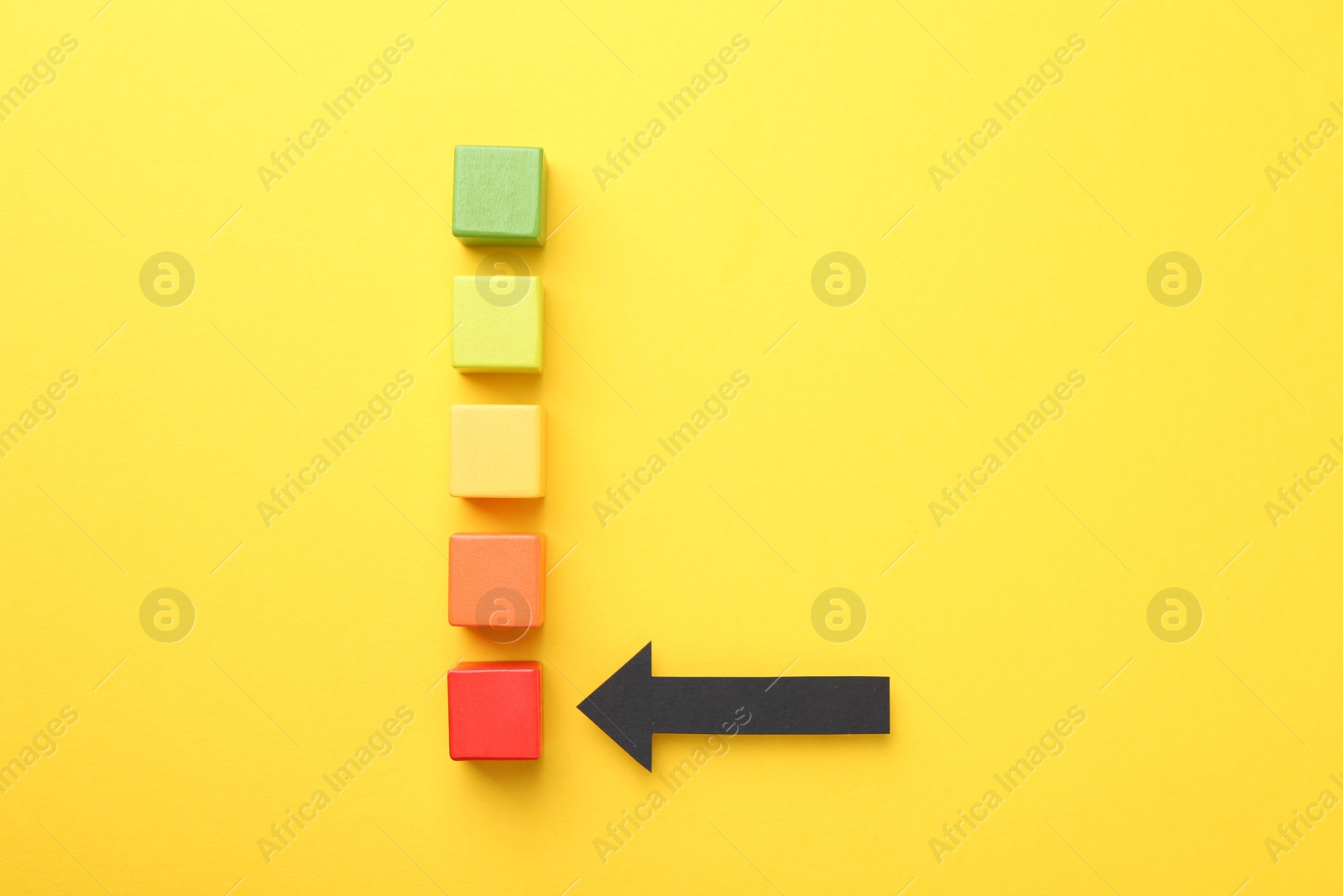 Maximum. Colorful cubes and arrow pointing at red one on yellow background, flat lay Photo of Maximum. Colorful cubes and arrow pointing at red one on yellow background, flat lay