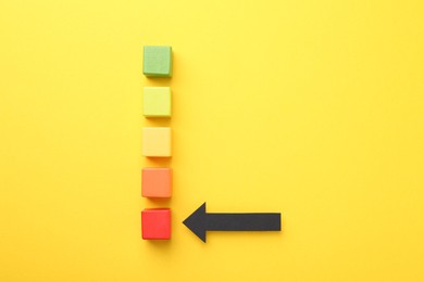 Photo of Maximum. Colorful cubes and arrow pointing at red one on yellow background, flat lay