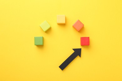Photo of Maximum. Colorful cubes and arrow pointing at red one on yellow background, flat lay