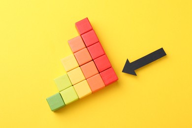 Photo of Maximum. Colorful cubes and arrow pointing at red one on yellow background, flat lay
