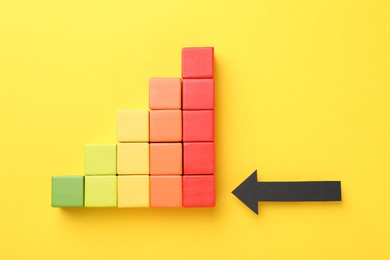 Photo of Maximum. Colorful cubes and arrow pointing at red one on yellow background, flat lay