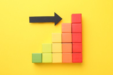 Photo of Maximum. Colorful cubes and arrow pointing at red one on yellow background, flat lay