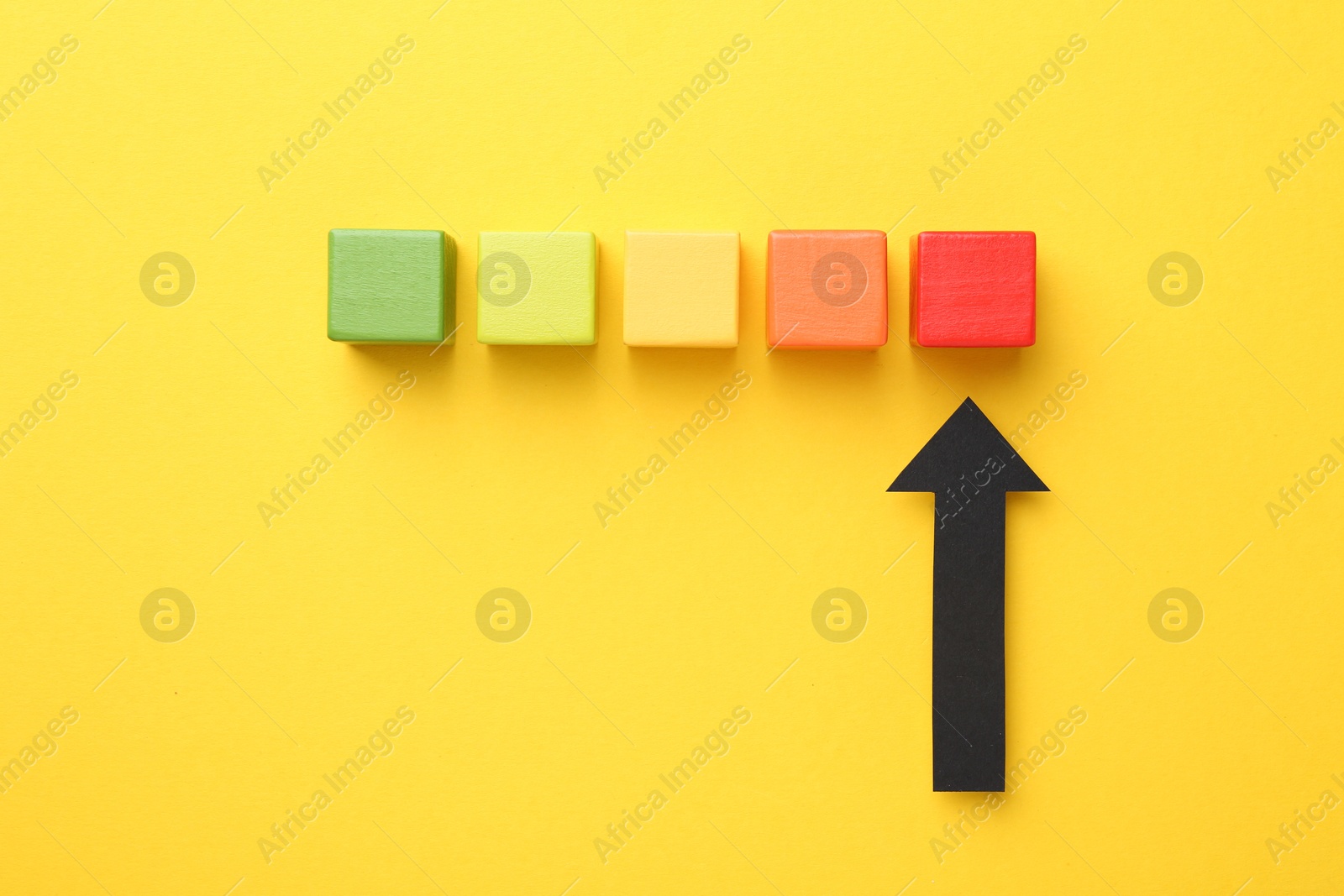 Maximum. Colorful cubes and arrow pointing at red one on yellow background, flat lay Photo of Maximum. Colorful cubes and arrow pointing at red one on yellow background, flat lay