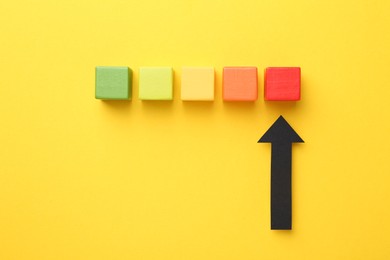 Photo of Maximum. Colorful cubes and arrow pointing at red one on yellow background, flat lay