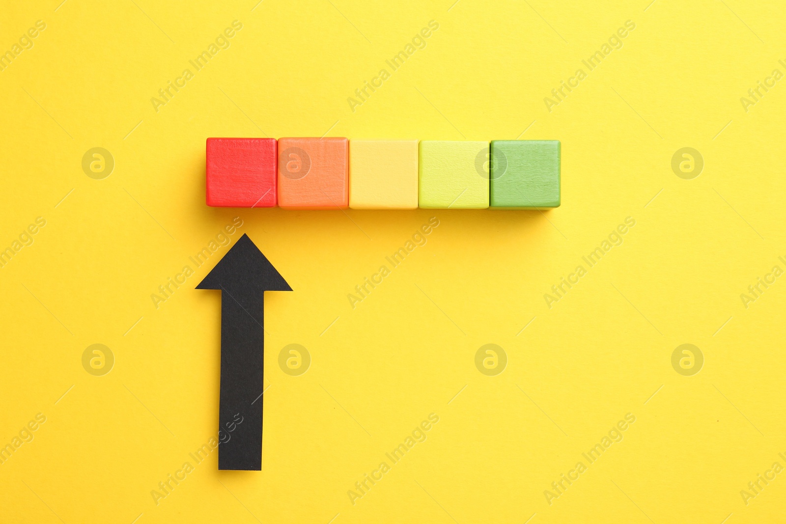 Maximum. Colorful cubes and arrow pointing at red one on yellow background, flat lay Photo of Maximum. Colorful cubes and arrow pointing at red one on yellow background, flat lay