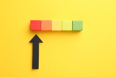Photo of Maximum. Colorful cubes and arrow pointing at red one on yellow background, flat lay