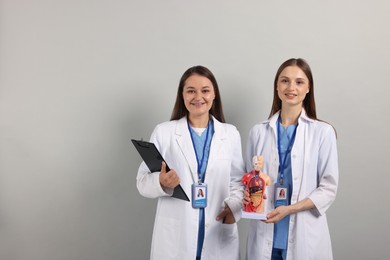 Photo of Medical students with human body model and clipboard on light grey background. Space for text