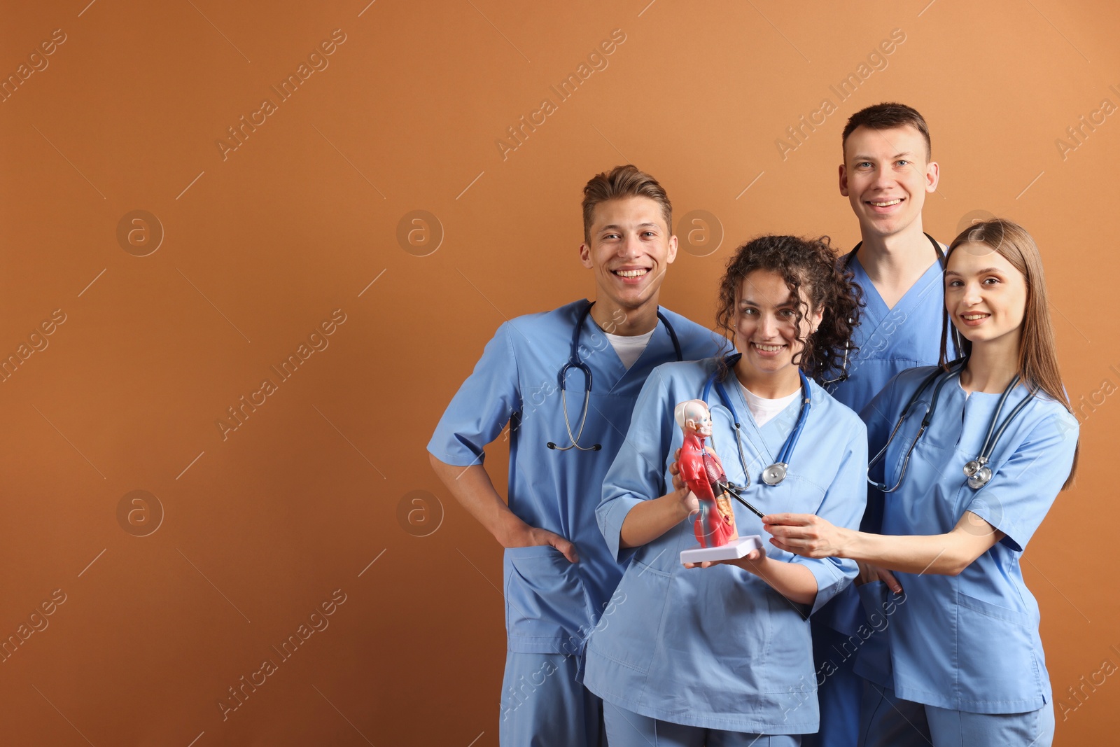 Photo of Group of medical students with human body model on brown background. Space for text