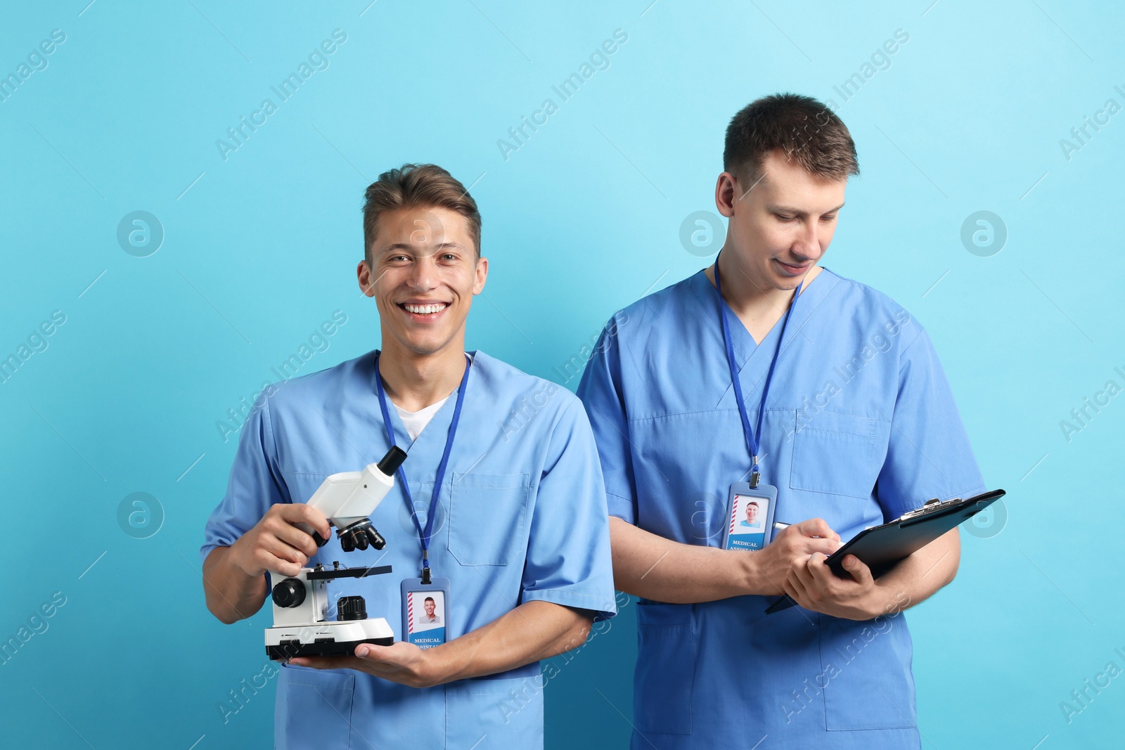 Photo of Medical students with microscope and clipboard on light blue background