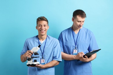 Photo of Medical students with microscope and clipboard on light blue background