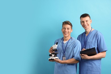 Photo of Medical students with microscope and clipboard on light blue background. Space for text