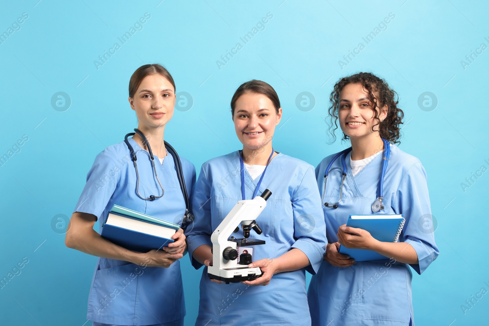 Photo of Group of medical students with microscope and books on light blue background