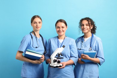 Photo of Group of medical students with microscope and books on light blue background