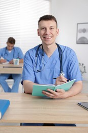 Photo of Medical students in uniforms studying at desks indoors, selective focus