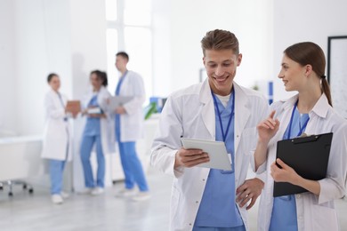 Photo of Medical students in uniforms with tablet and clipboard indoors, selective focus