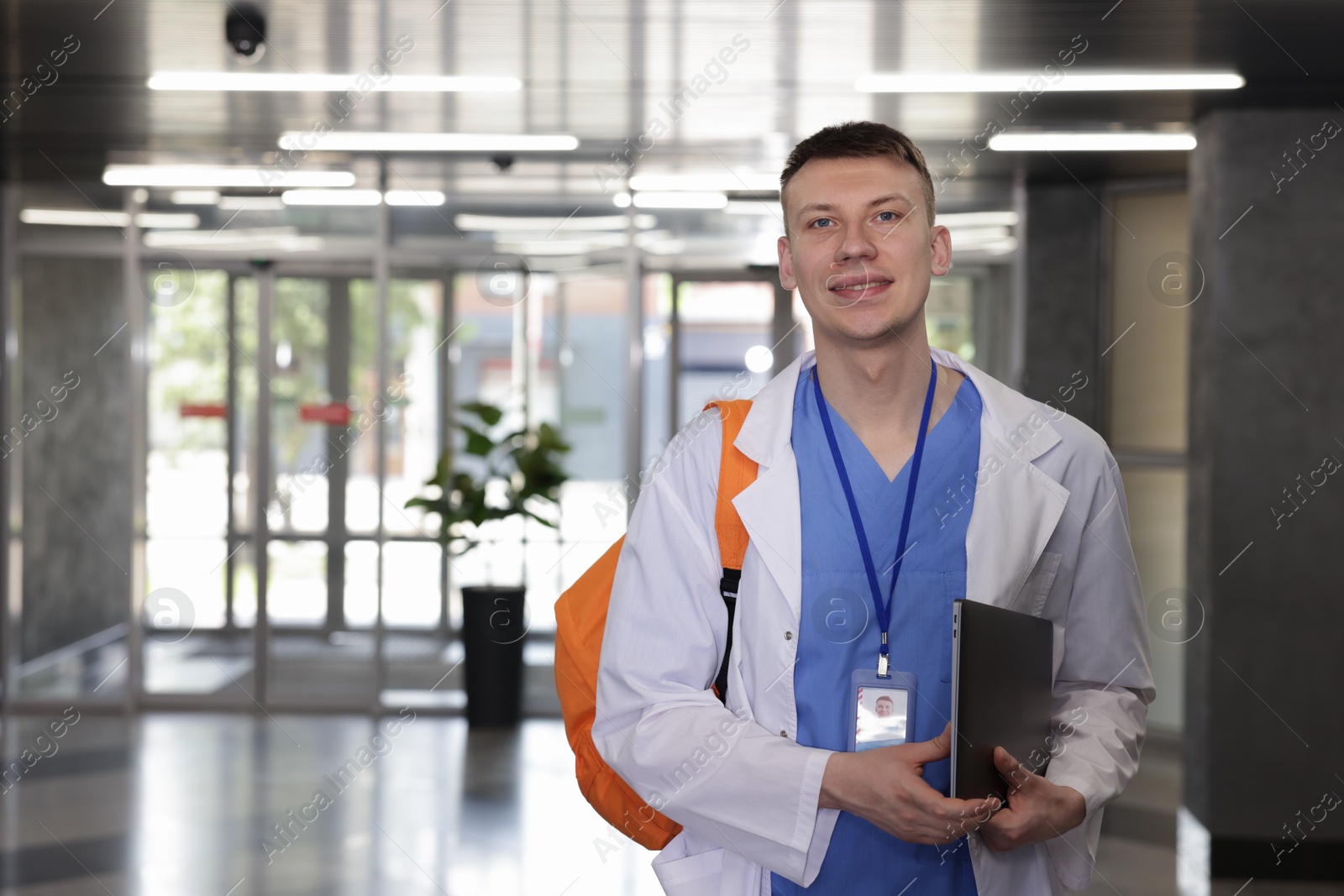 Photo of Medical student in uniform with backpack and laptop indoors, space for text