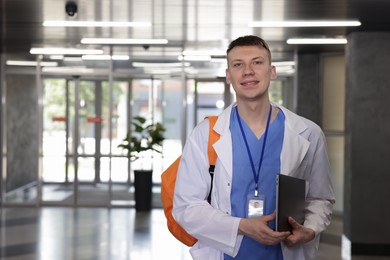 Photo of Medical student in uniform with backpack and laptop indoors, space for text