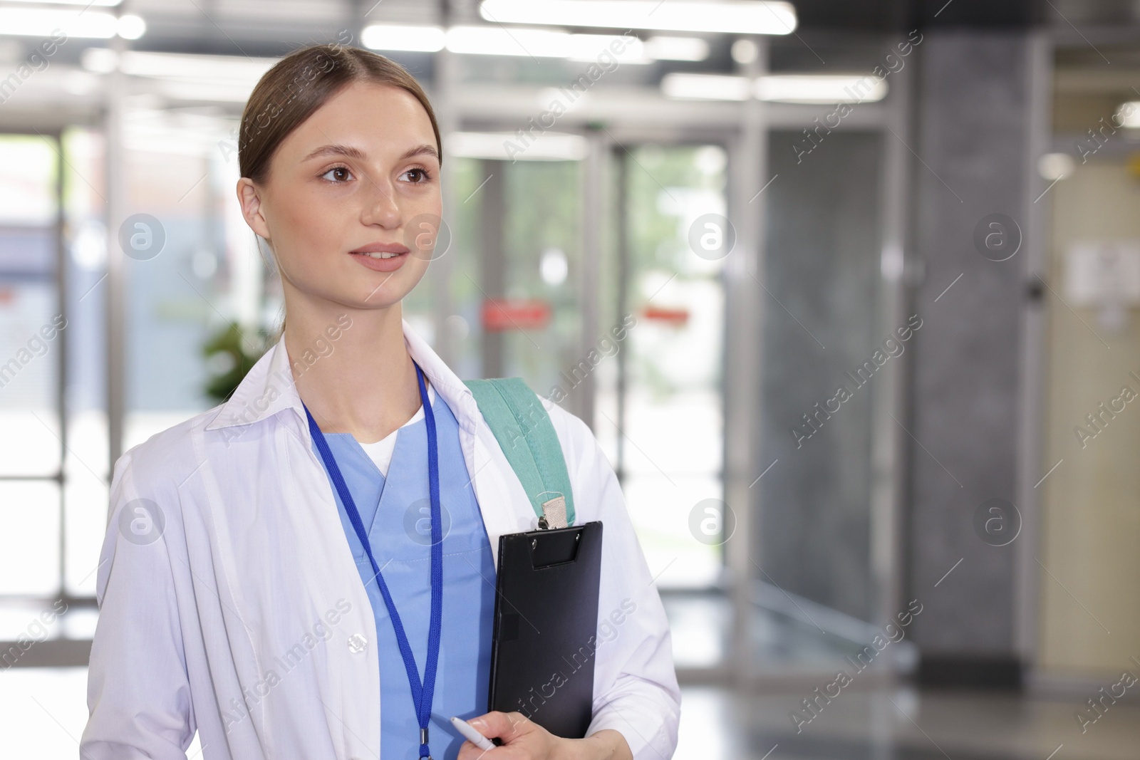 Photo of Medical student in uniform with backpack and clipboard indoors, space for text