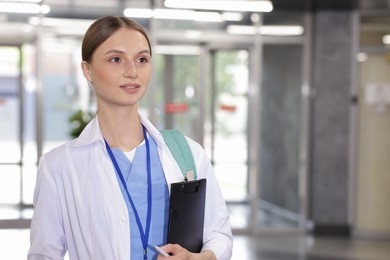 Photo of Medical student in uniform with backpack and clipboard indoors, space for text