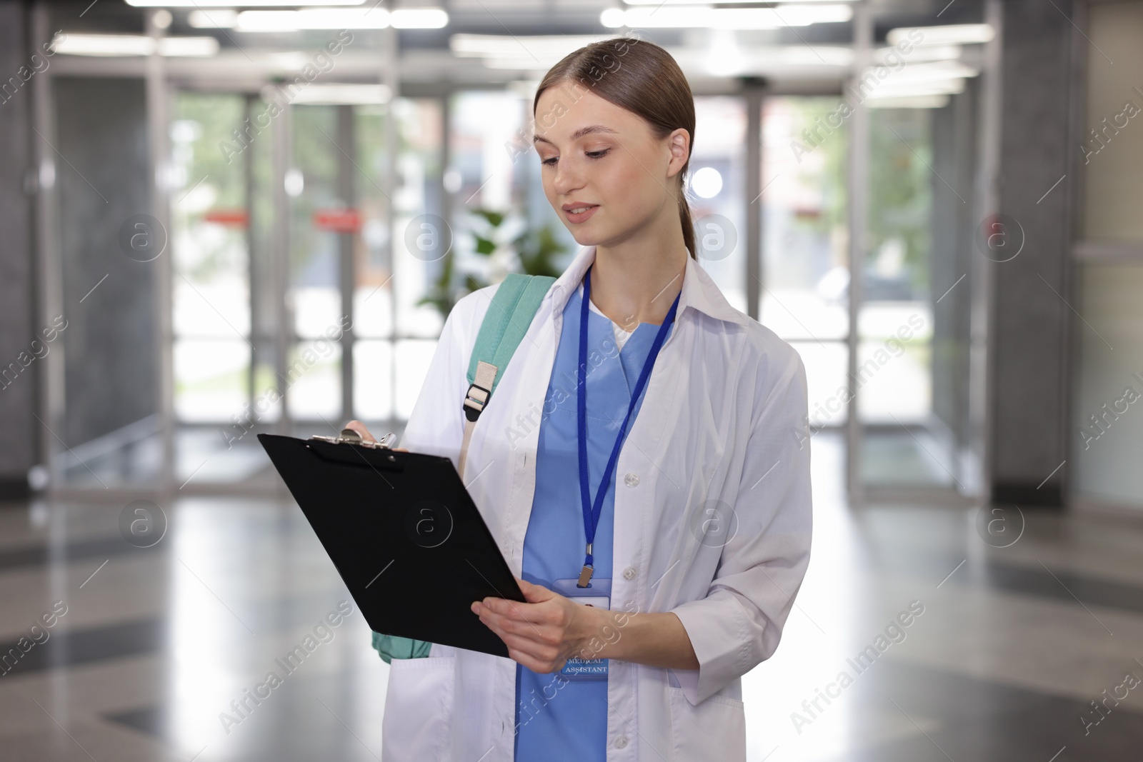 Photo of Medical student in uniform with backpack and clipboard indoors