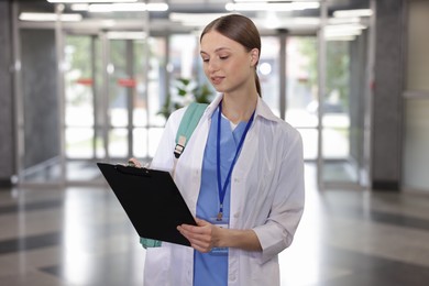 Photo of Medical student in uniform with backpack and clipboard indoors